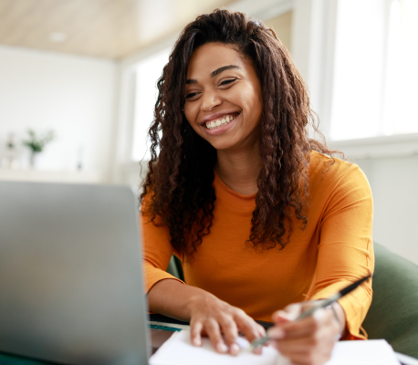 happy woman writing notes and looking at laptop